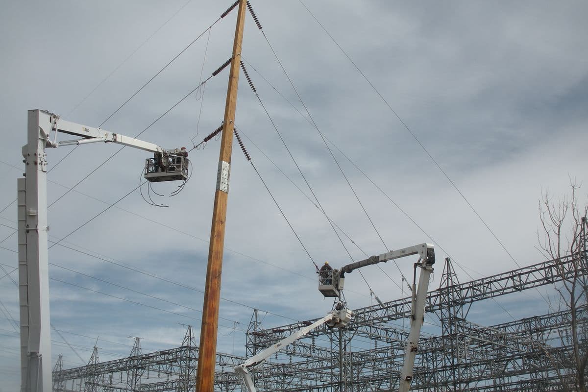 Linemen and electricians in two bucket trucks connect lines to a tall wooden pole at a substation in Williston, North Dakota.