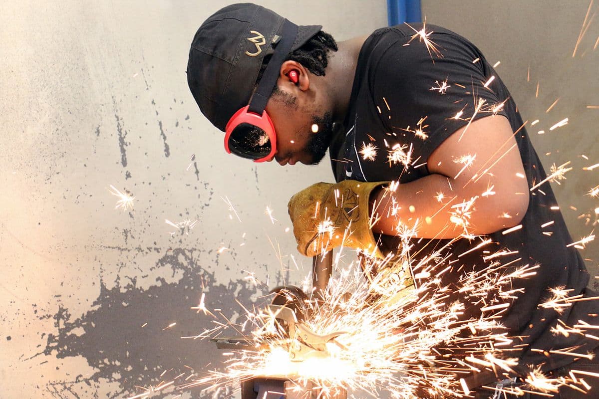 A welding student in ear protection shapes a piece of metal with a grinder as sparks fly in a college shop in Dade City, Florida.