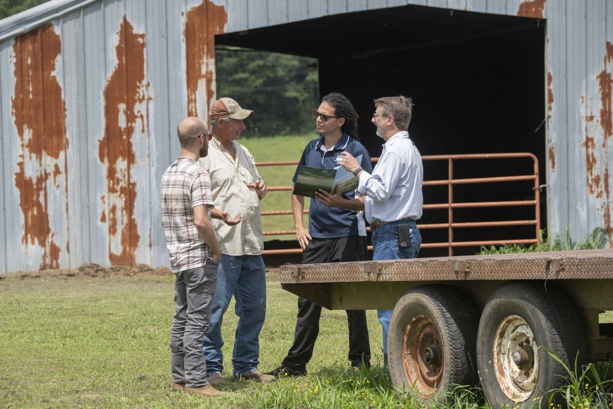 A farmer talks through his plans with three conservation staff beside a barn and a flatbed trailer in Hector, Arkansas.