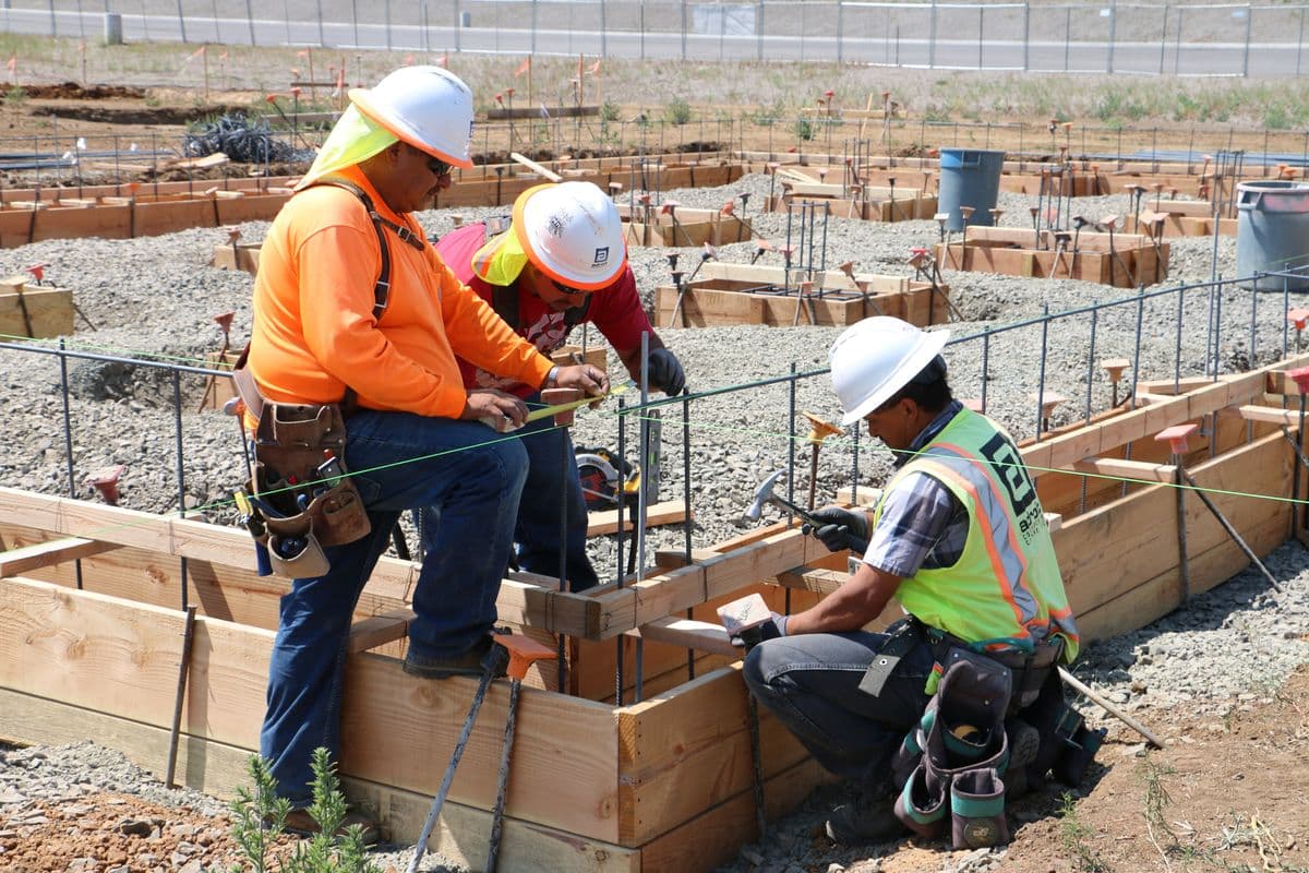 Three construction workers in hard hats check the forms for a foundation before a concrete pour in Oregon.